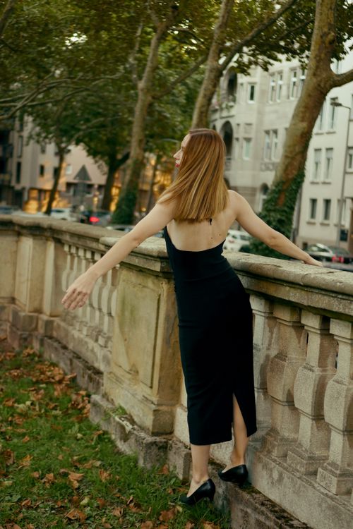 Free Stylish woman in black dress poses by stone railing in city park, embracing nature. Stock Photo