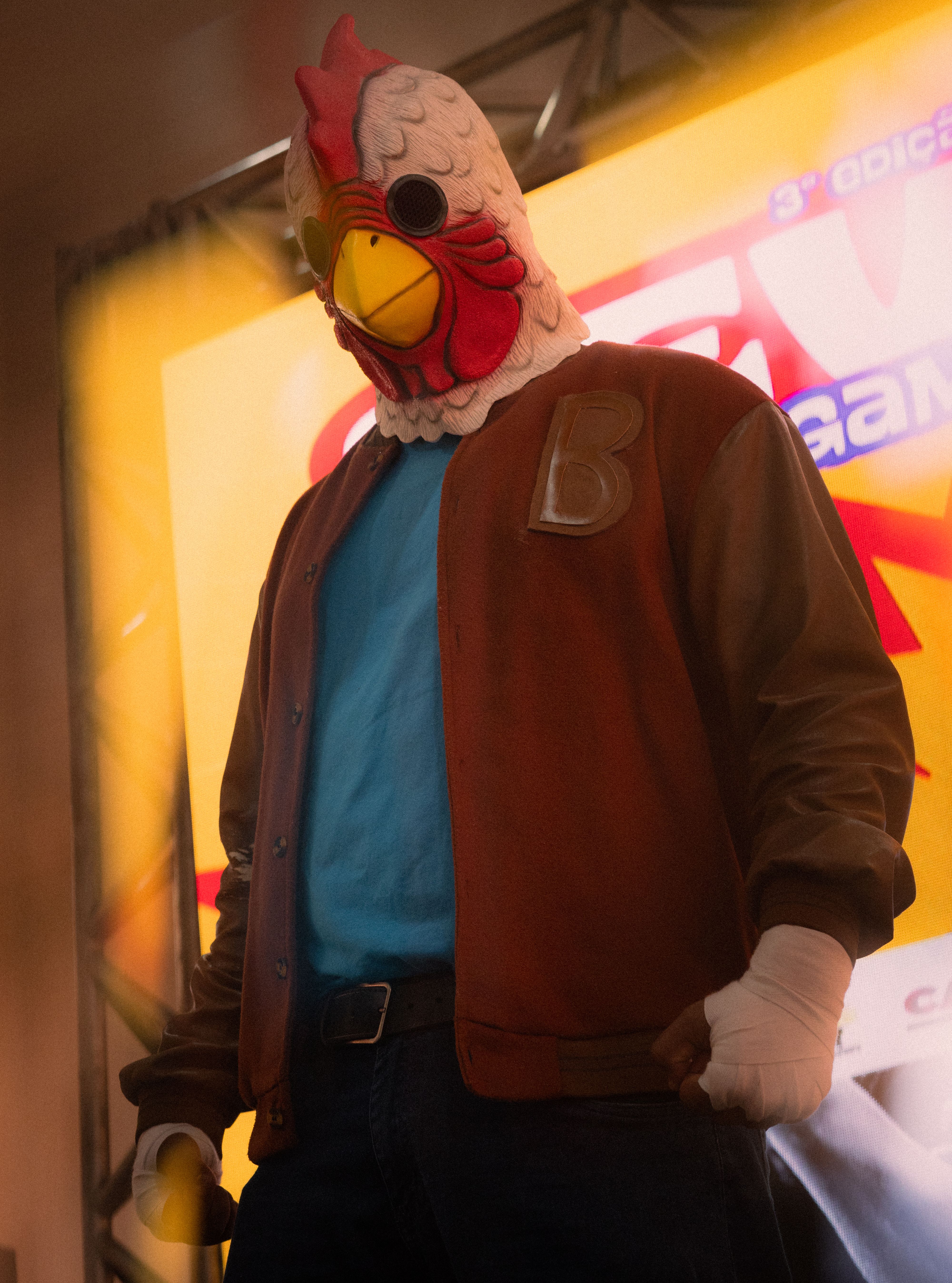 Cosplay of a character wearing a chicken mask and jacket at a vibrant event.