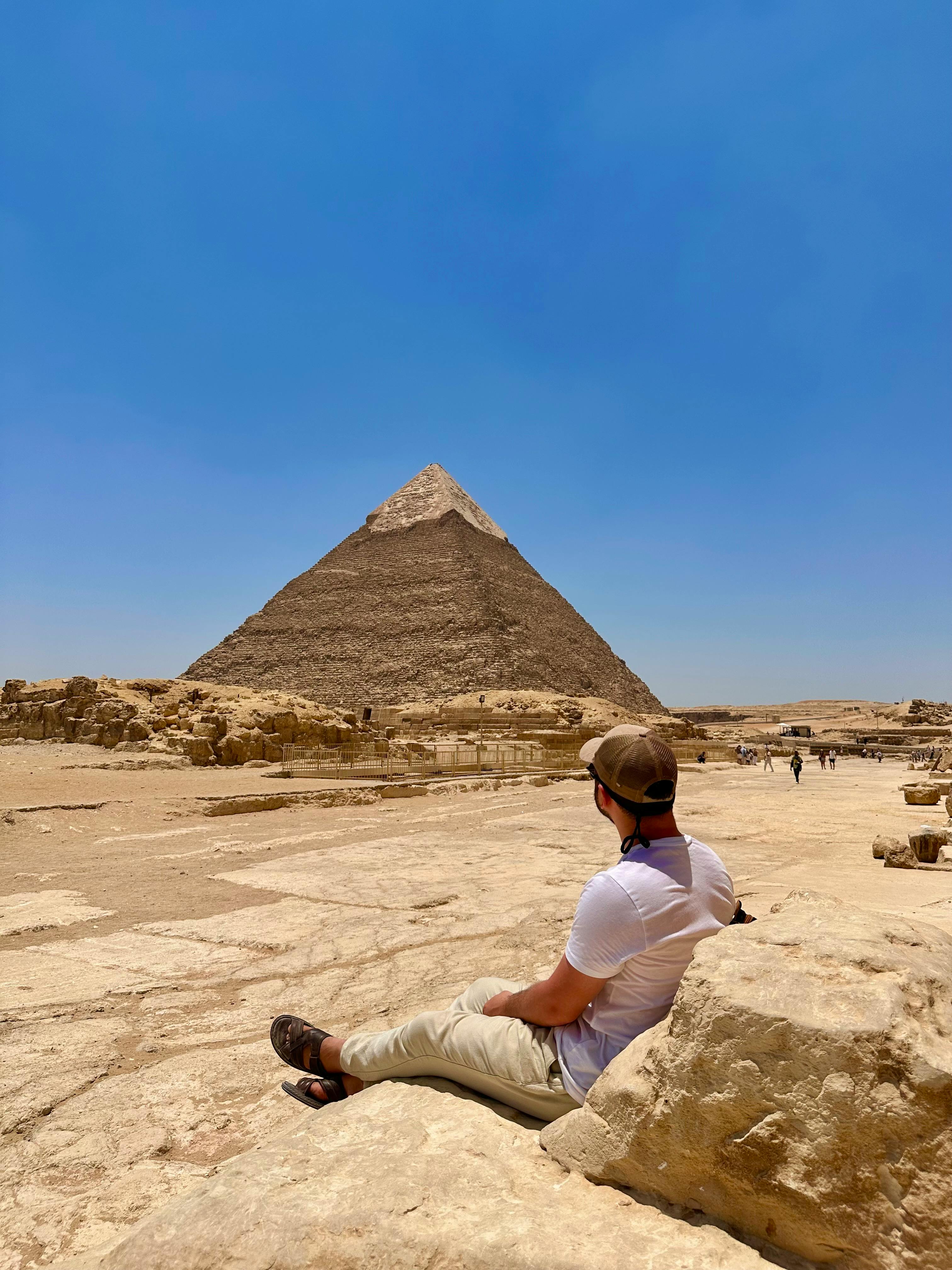 在阳光明媚的一天，一个人坐在吉萨大金字塔前欣赏它