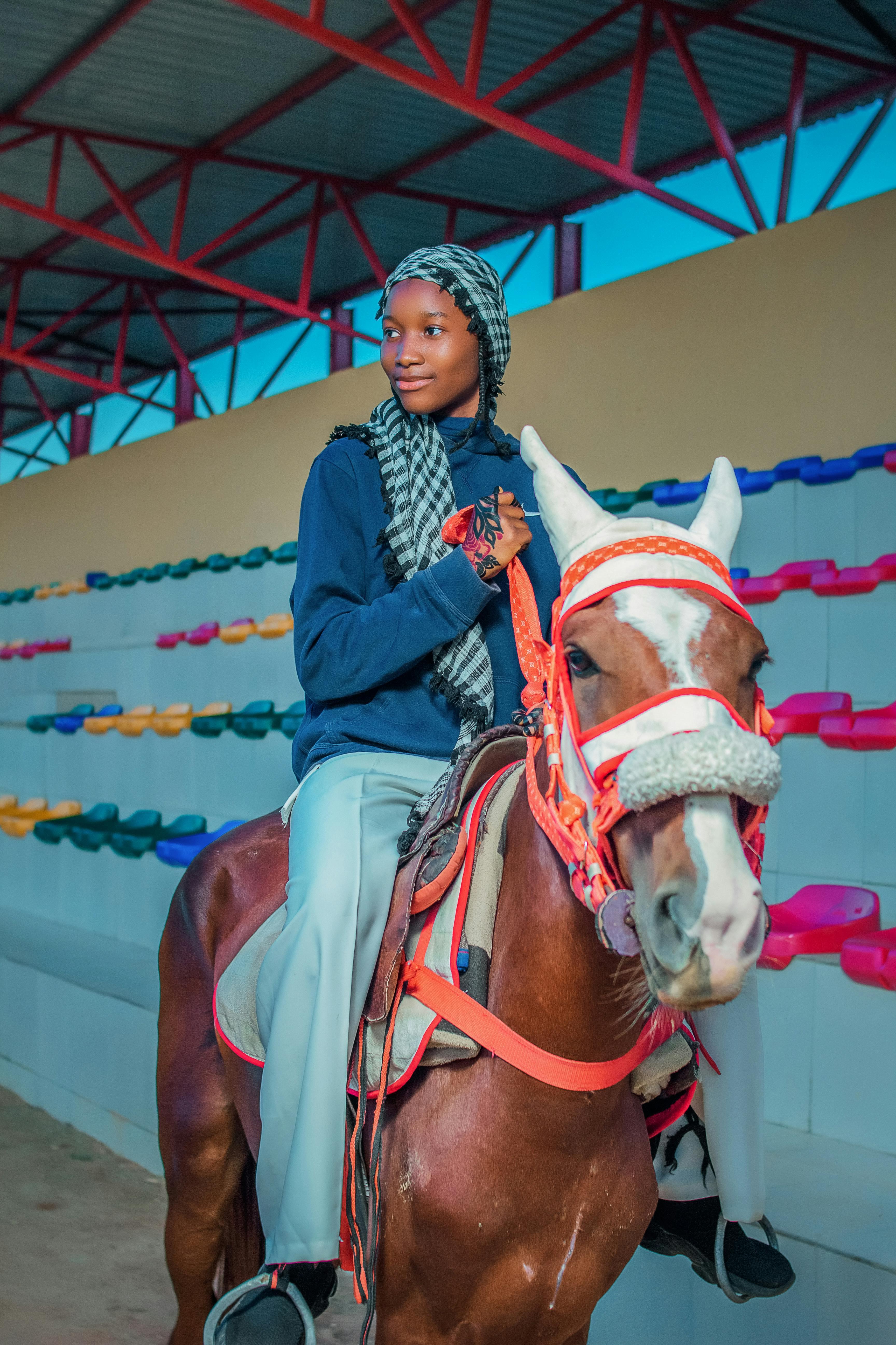 A woman enjoys horseback riding in a colorful indoor arena setting.