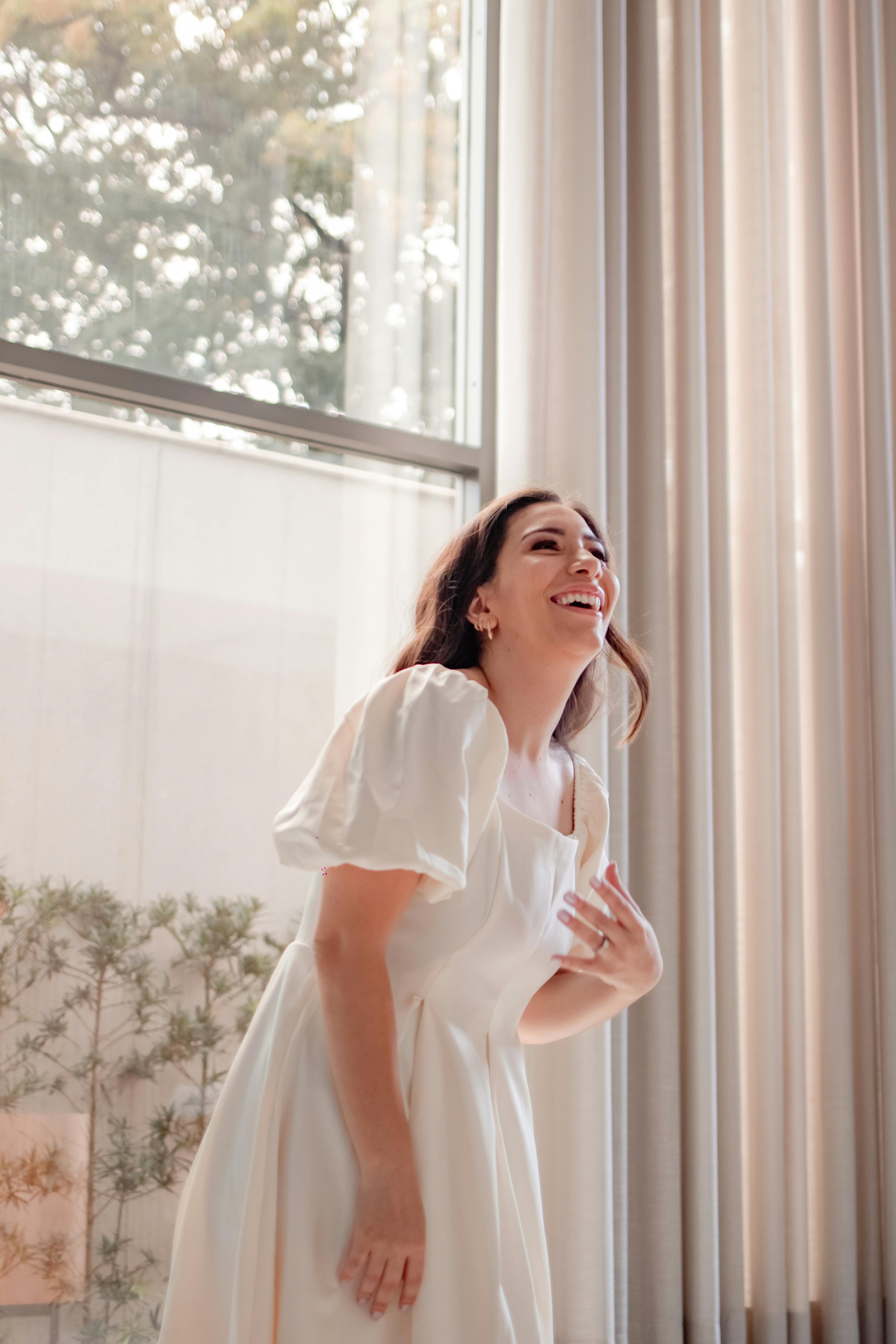 身着白色连衣裙的女子在阳光明媚的房间里欢笑，营造出温暖无忧无虑的氛围