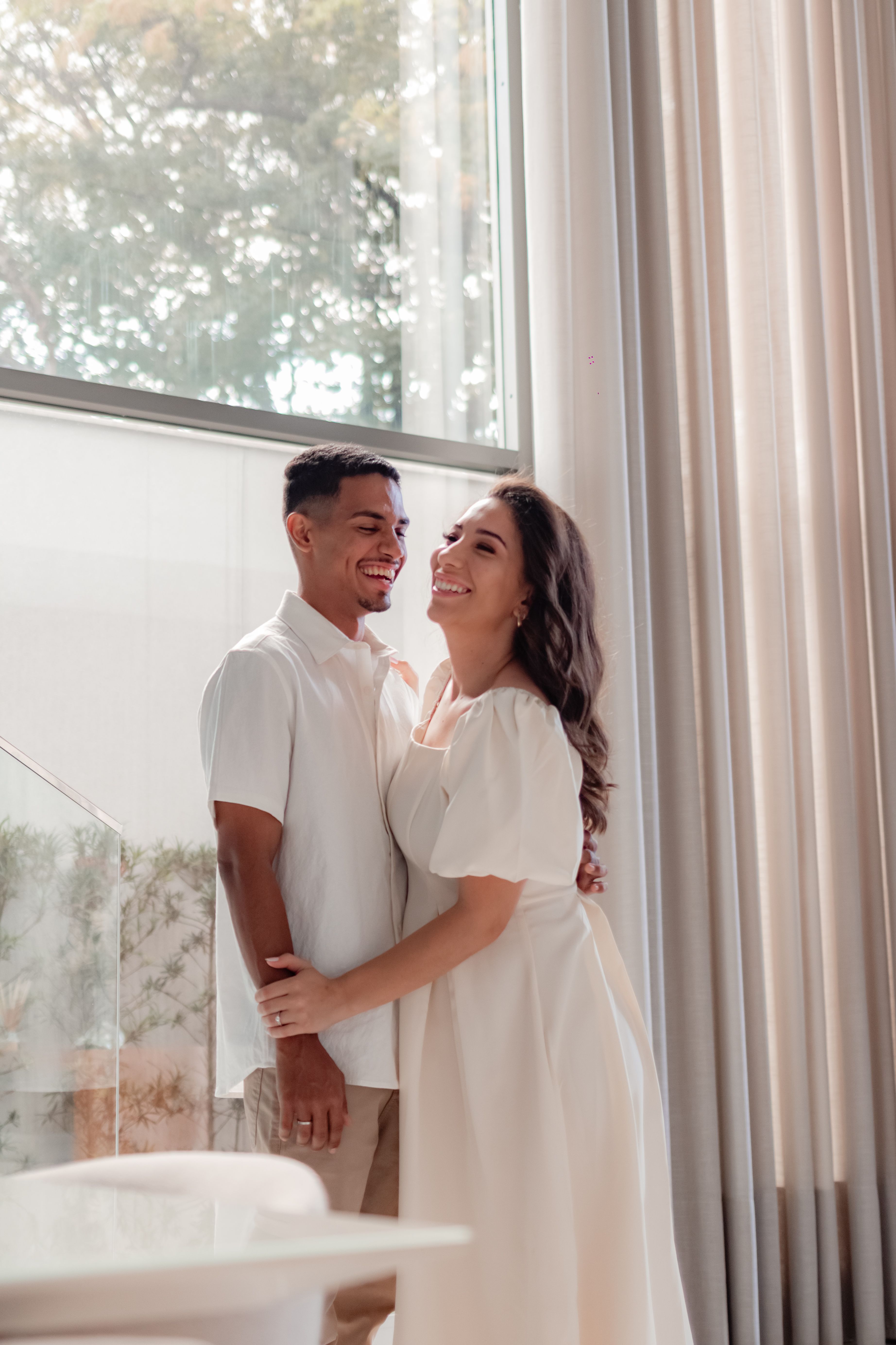 A happy couple sharing a warm moment beside a large window with natural light.
