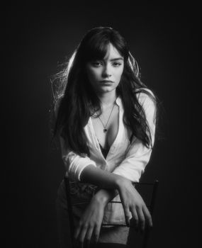Intimate black and white portrait of a woman seated on a chair in a classic pose.