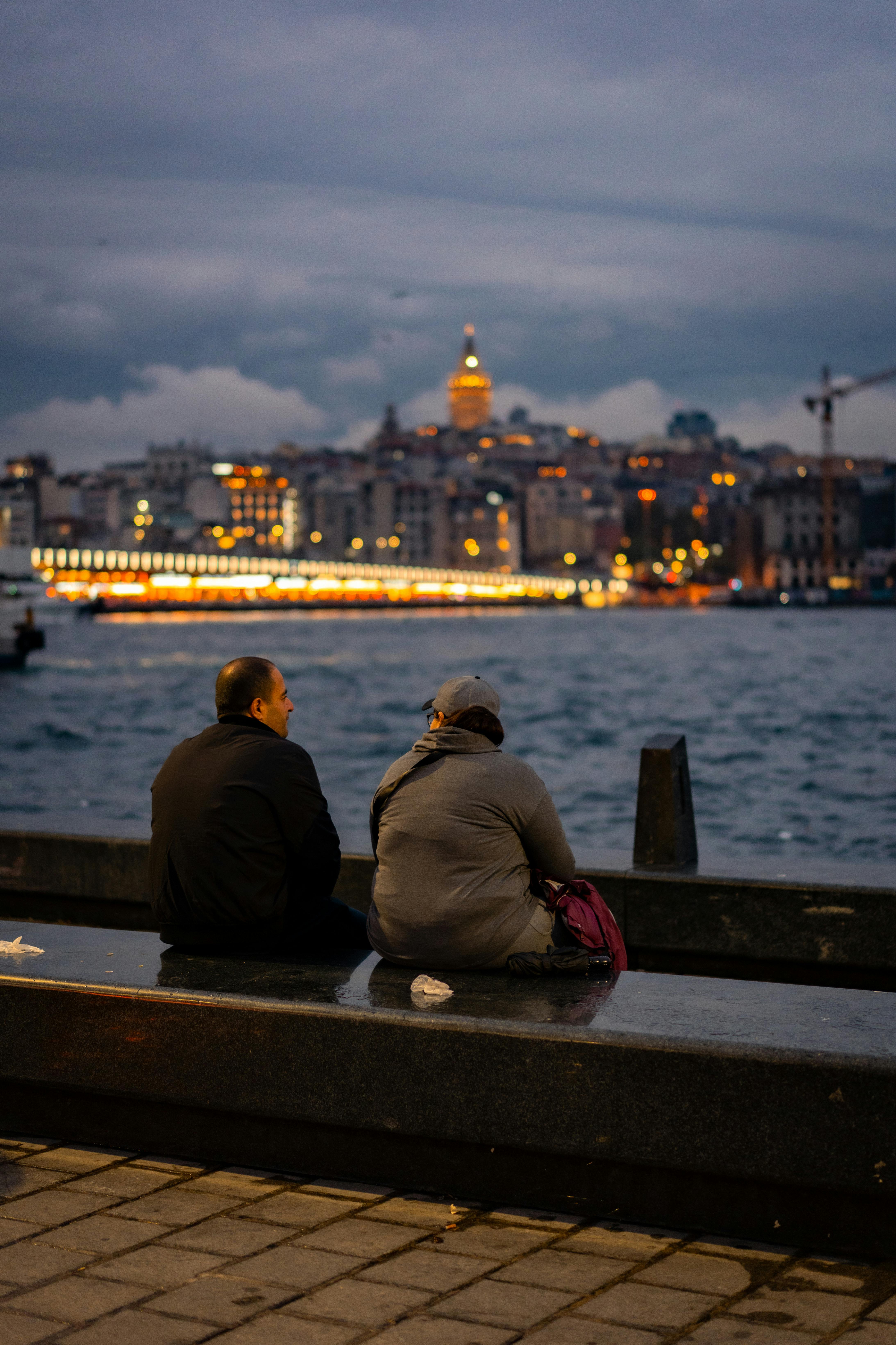 两个人坐在伊斯坦布尔海滨，背后是加拉塔塔
