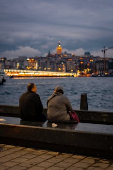 两个人坐在伊斯坦布尔海滨，背后是加拉塔塔