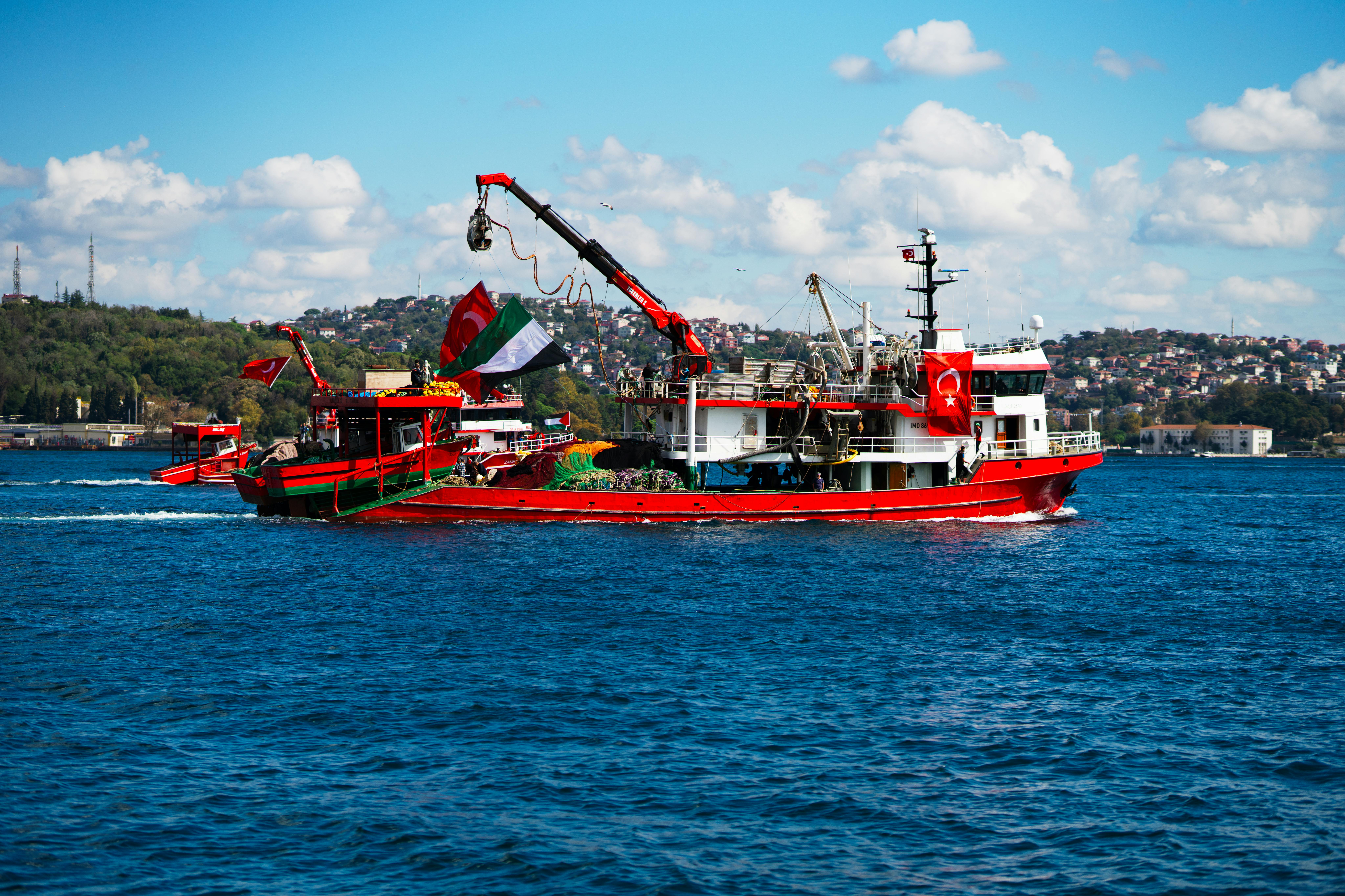 在土耳其伊斯坦布尔，一艘充满活力的红色渔船在蔚蓝的天空下航行在博斯普鲁斯海峡上