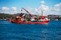 在土耳其伊斯坦布尔，一艘充满活力的红色渔船在蔚蓝的天空下航行在博斯普鲁斯海峡上