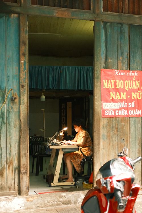 Free A woman sewing in a cozy, rustic workshop in Jakarta, Indonesia, with vibrant street life and cultural elements. Stock Photo