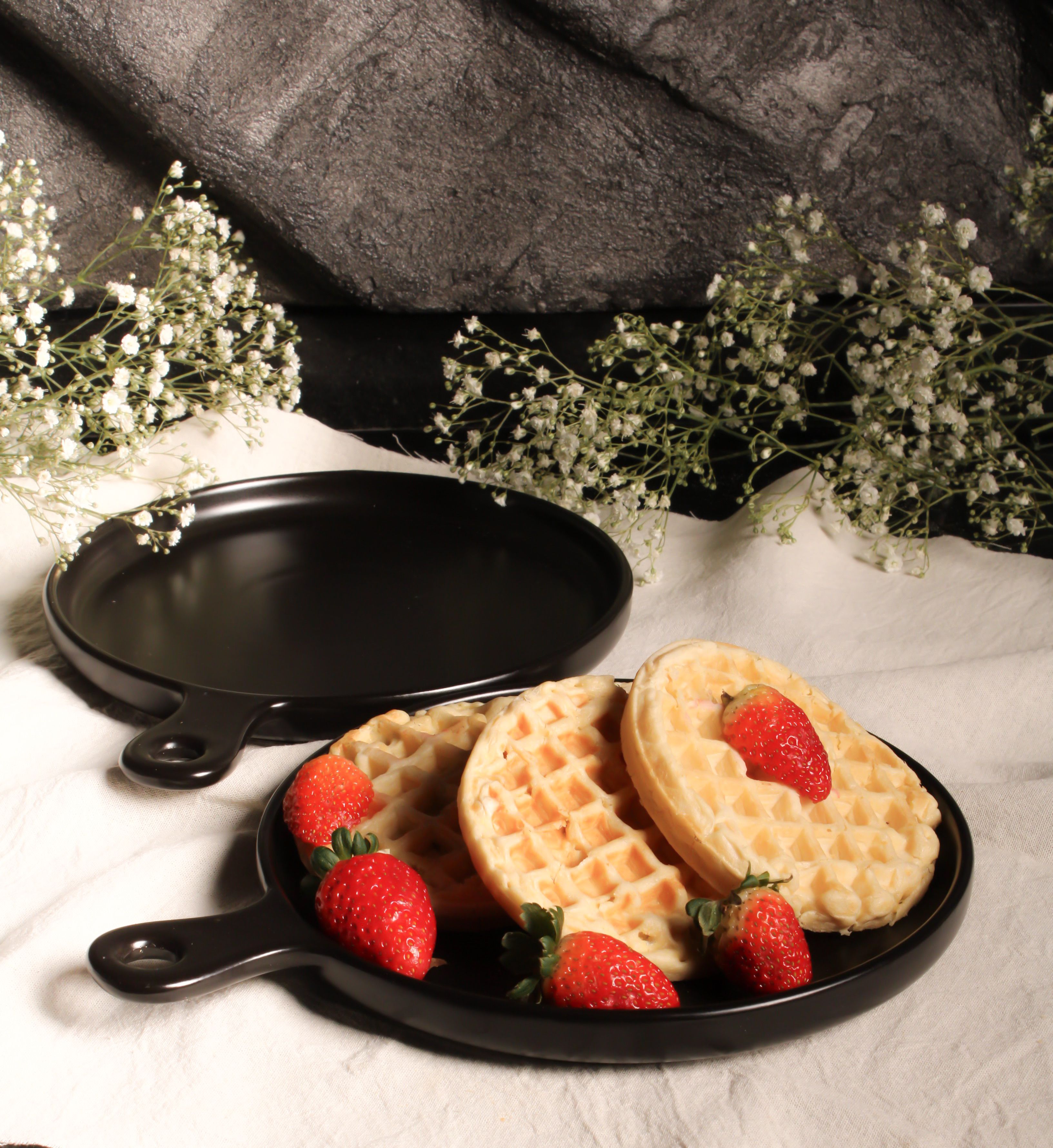 Crispy waffles with fresh strawberries served on black plates with floral decorations.