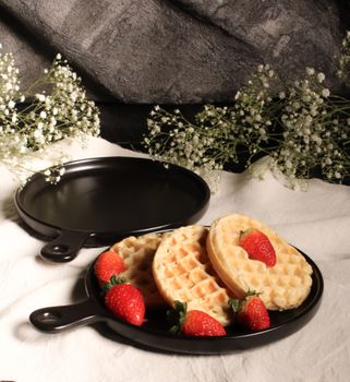 Crispy waffles with fresh strawberries served on black plates with floral decorations.
