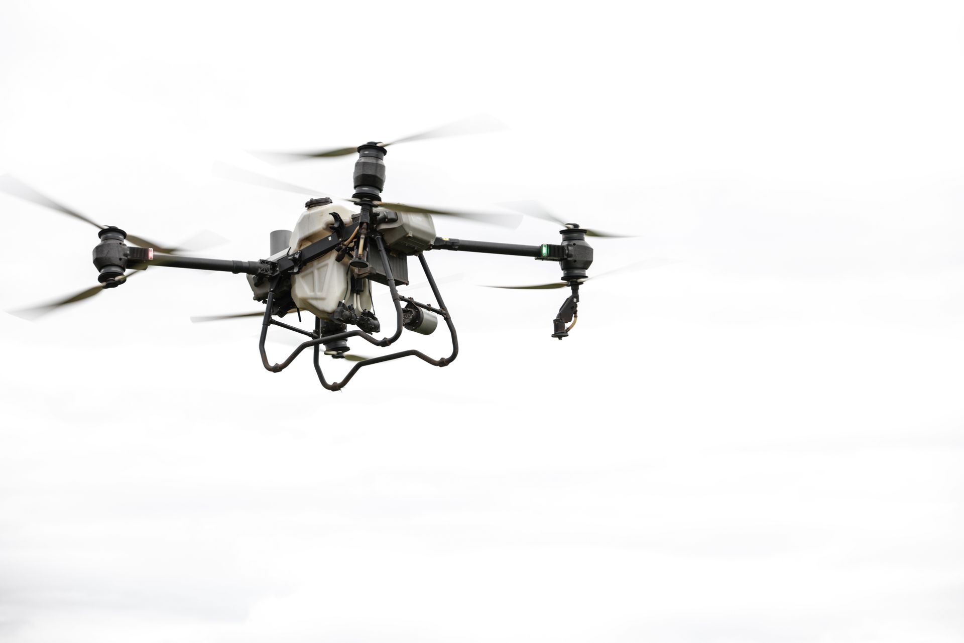 A surveillance drone flying against a grey, overcast sky