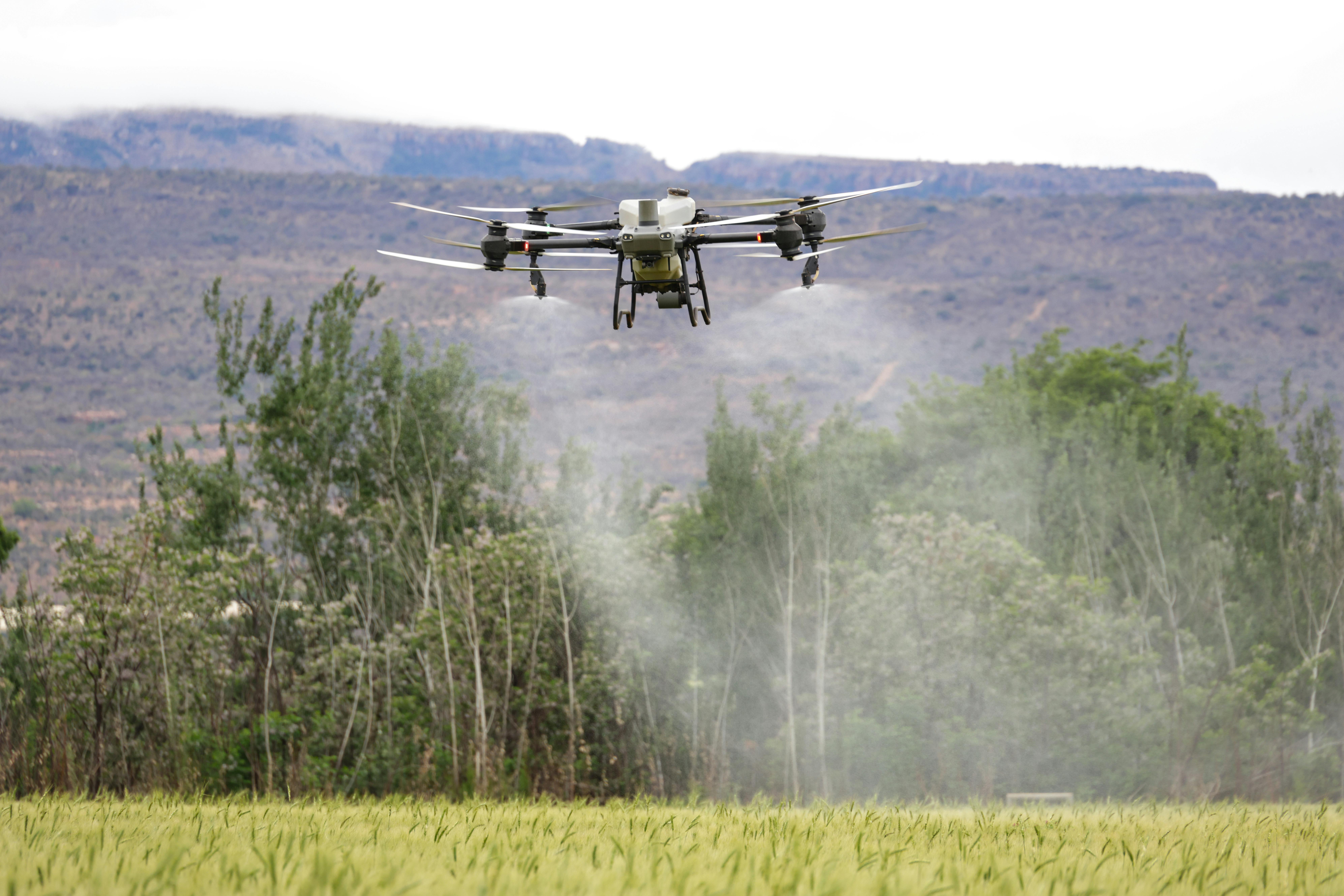High-tech drone spraying crops in a field with mountains in the background, showcasing modern farming technology.