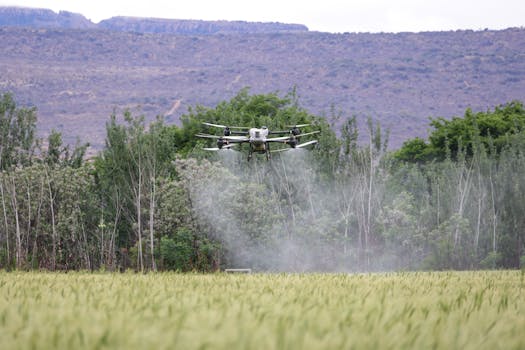 Aerial drone spraying pesticides on a crop field against a lush green landscape.