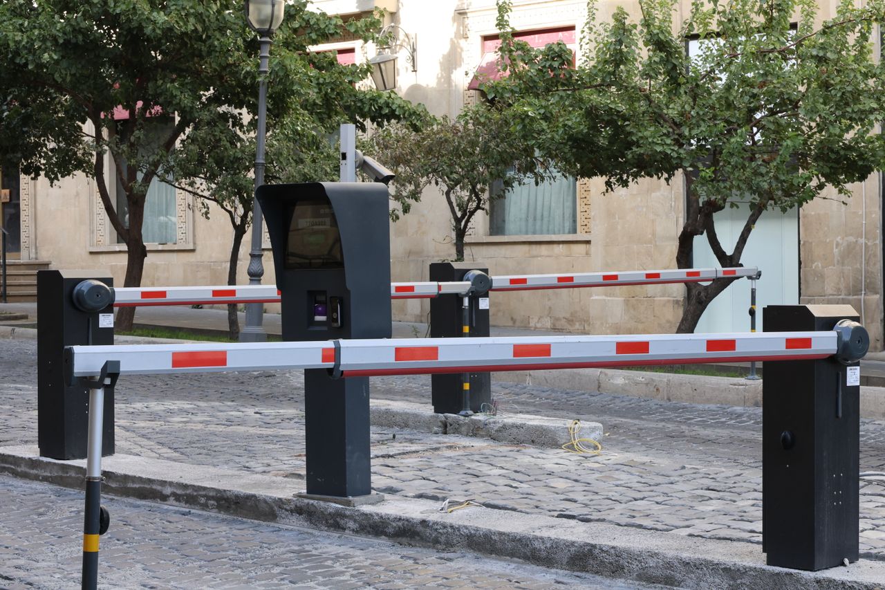 Modern parking barrier gate system on cobblestone street with greenery