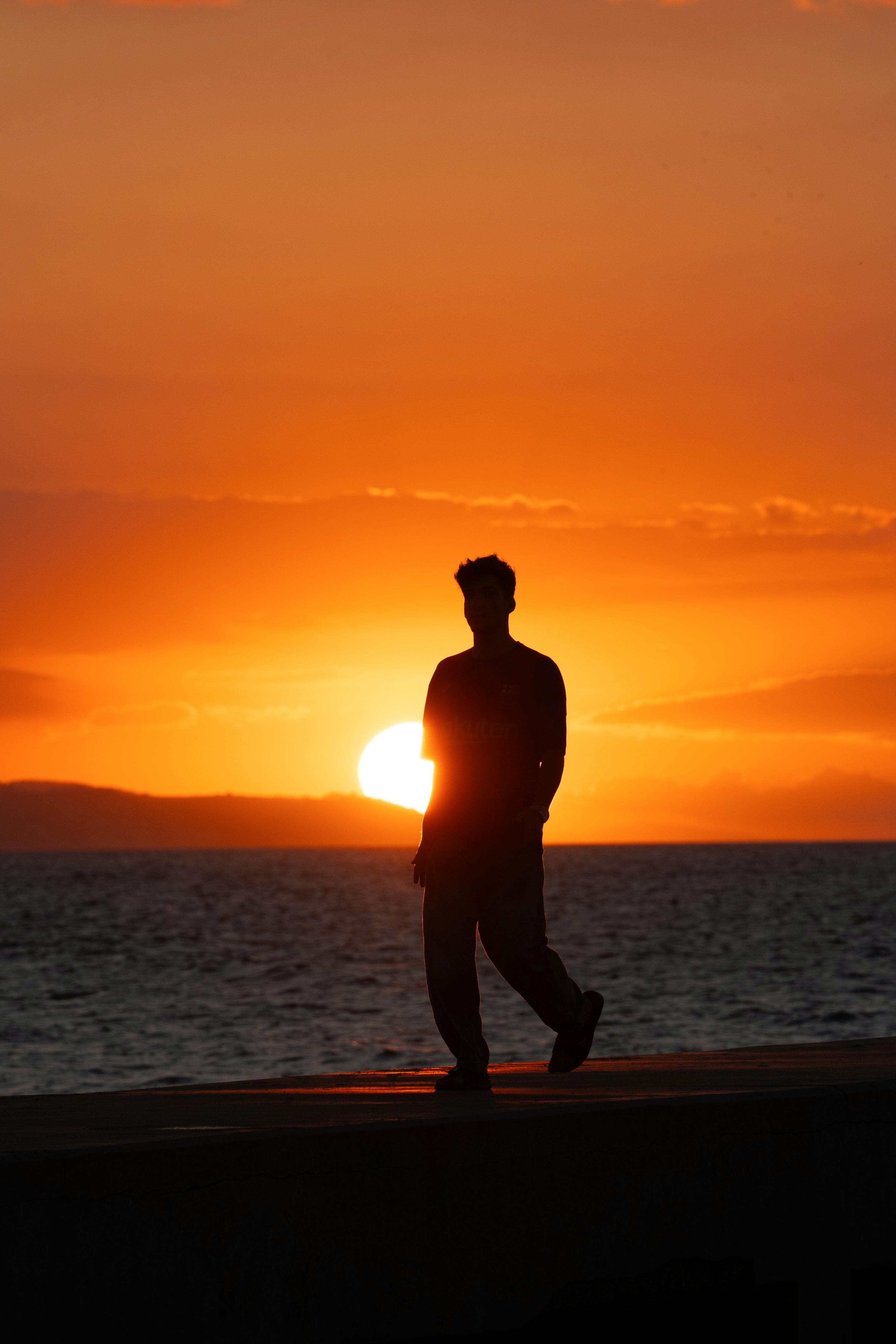 一个人在日落时分沿着海岸线行走，剪影映衬着海洋的活力