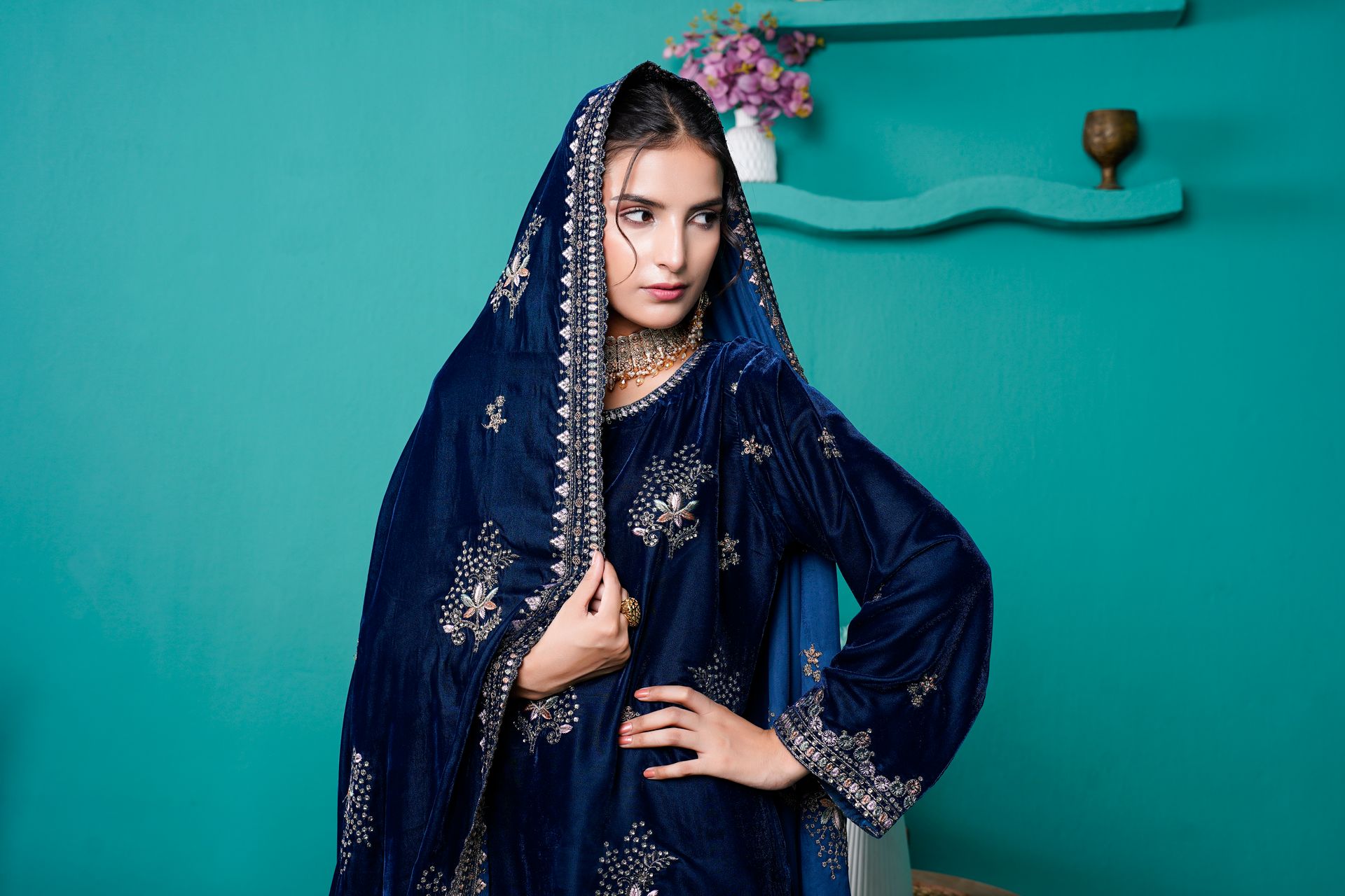 Model in a blue embroidered velvet dress showcasing eastern fashion indoors.