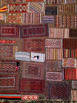 A top-down view of various traditional rugs arranged on the ground, showcasing vibrant patterns and colors.