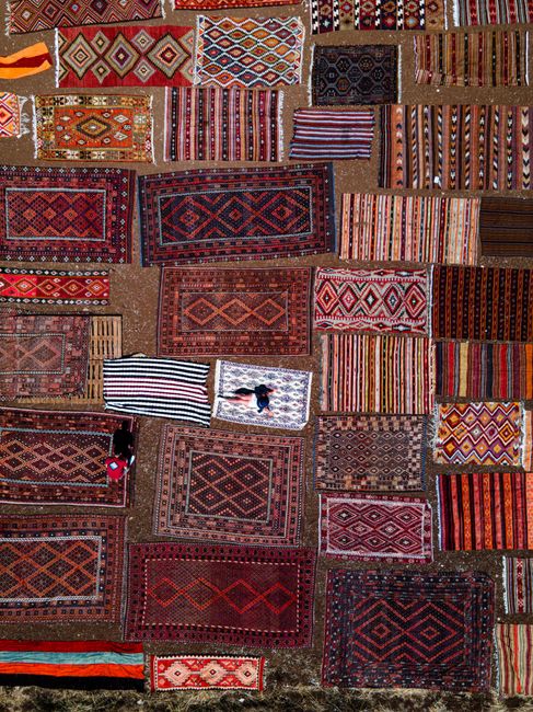 A top-down view of various traditional rugs arranged on the ground, showcasing vibrant patterns and colors.