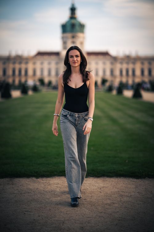 Free A woman confidently walks towards the camera with a historic building in the background. Stock Photo
