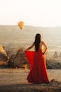 一名穿着红色连衣裙的女子站在图尔基耶卡帕多西亚的户外，观赏着日出时分的热气球