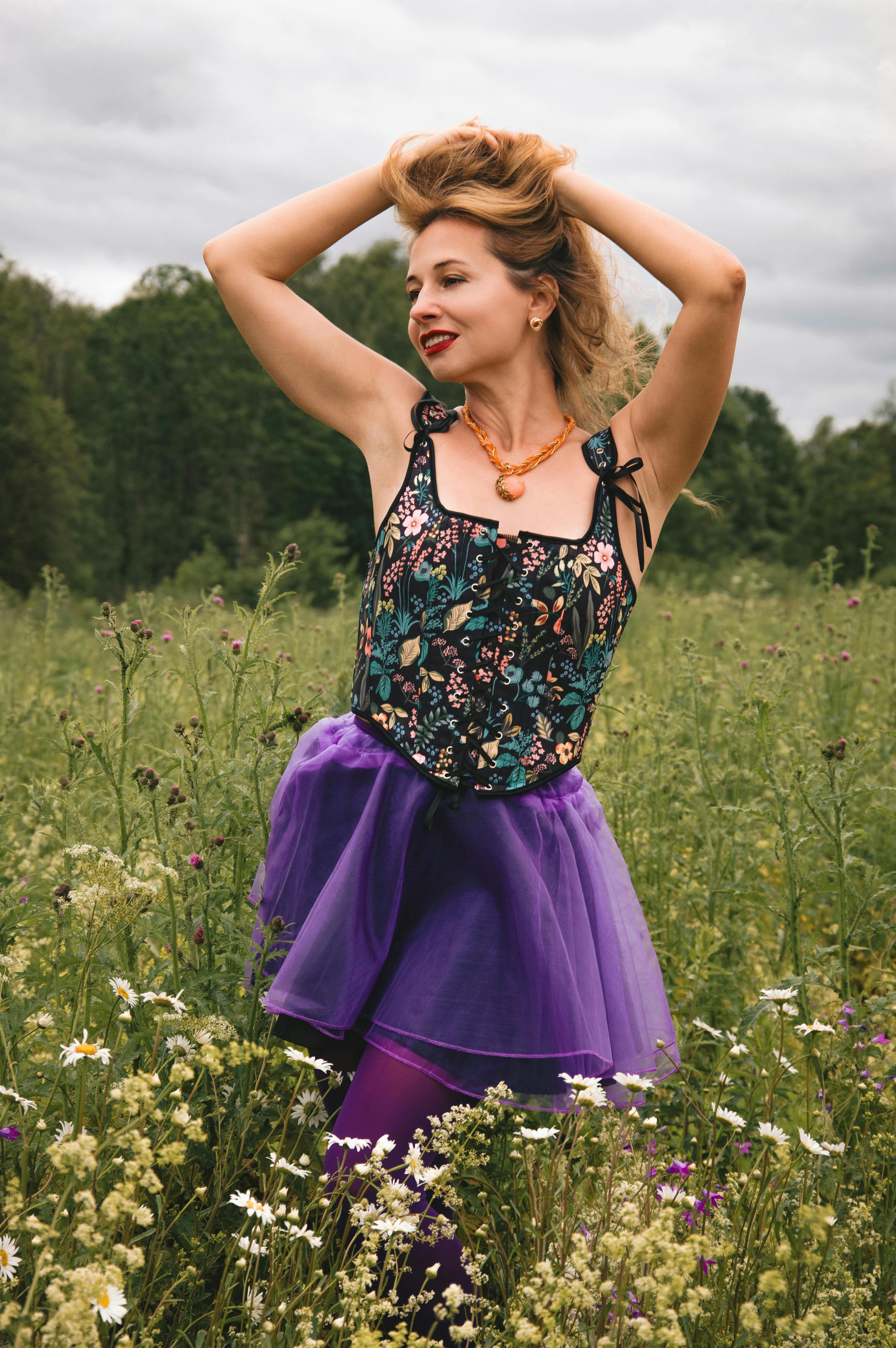 女子身穿彩色花卉连衣裙和紫色裙子，在夏季草地上快乐地摆姿势