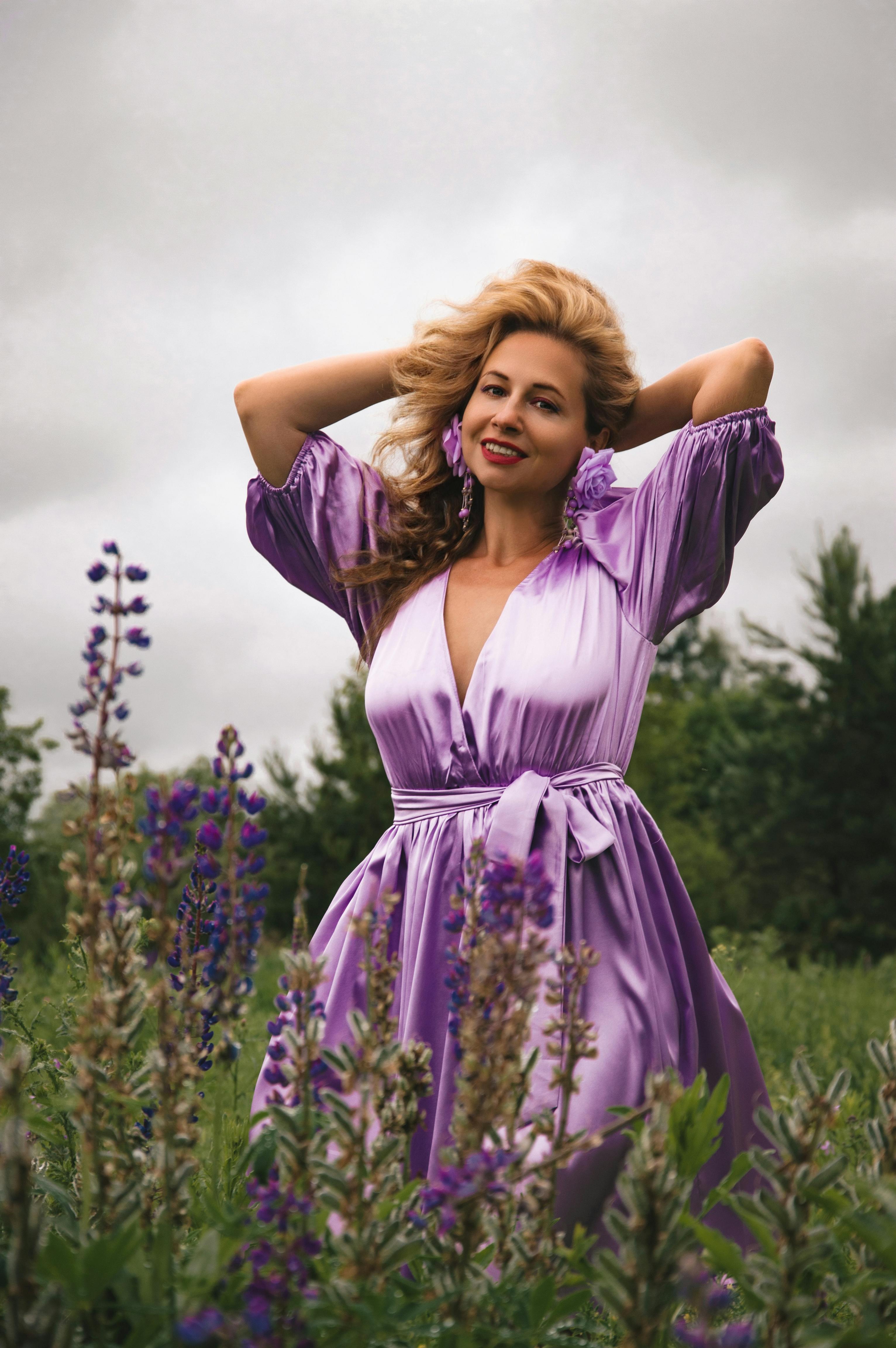 身着淡紫色连衣裙的女人在郁郁葱葱的花田中优雅地摆姿势，流露出自信和快乐
