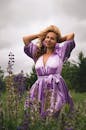 身着淡紫色连衣裙的女人在郁郁葱葱的花田中优雅地摆姿势，流露出自信和快乐