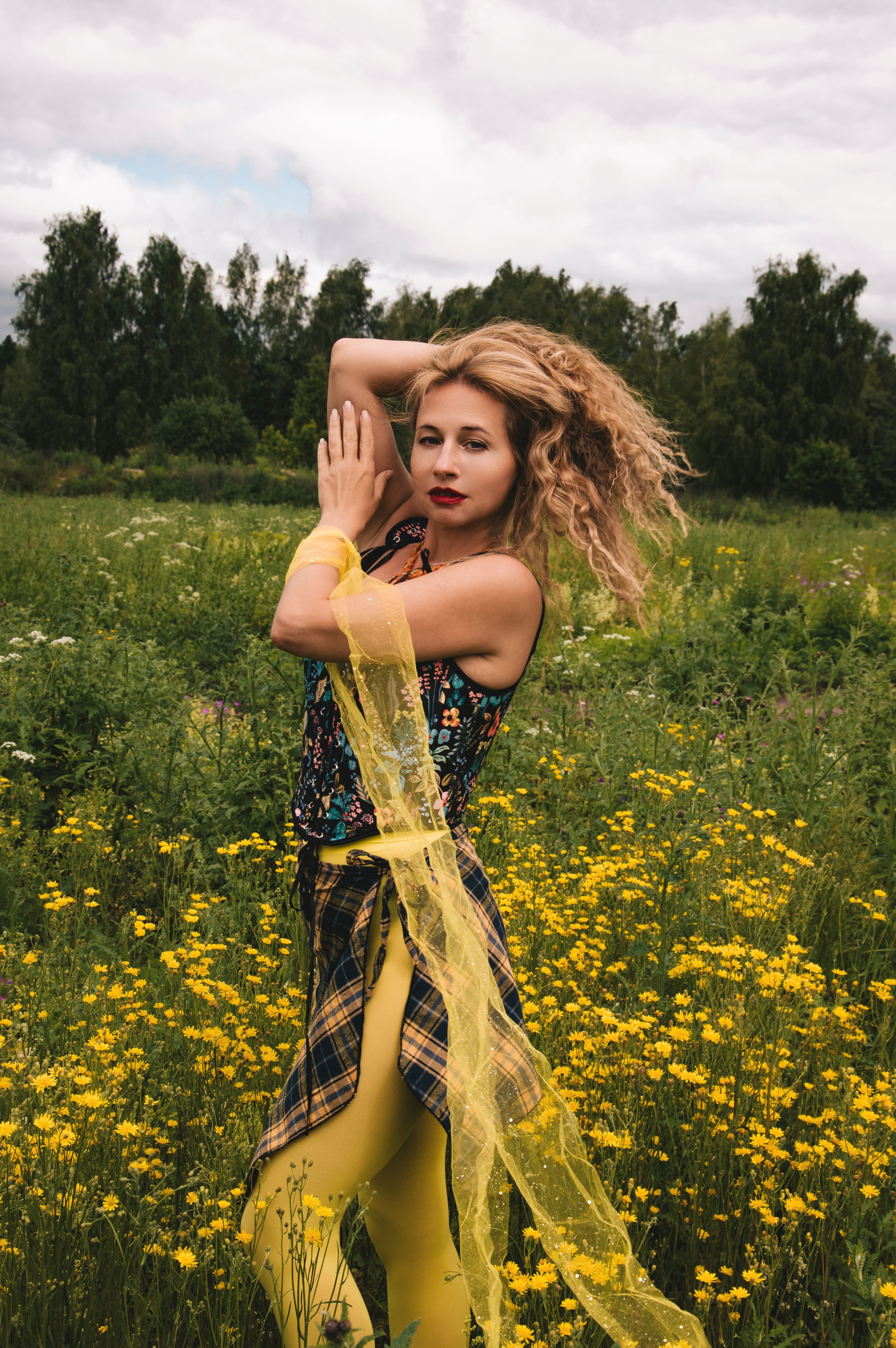 Woman with curly hair poses amidst vibrant yellow flowers, capturing a natural and artistic vibe.