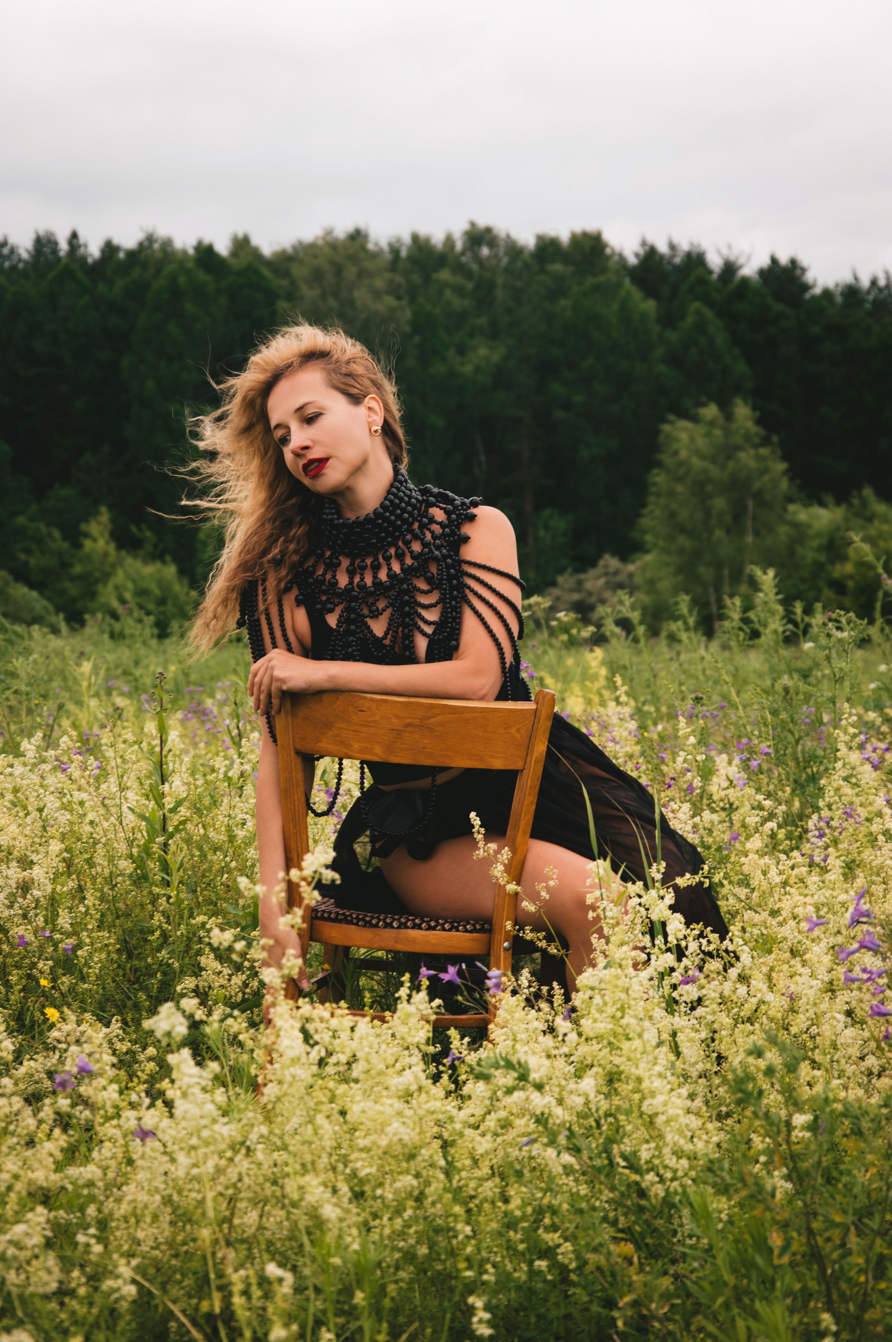 A woman in a black dress sits gracefully in a lush, flowering meadow.