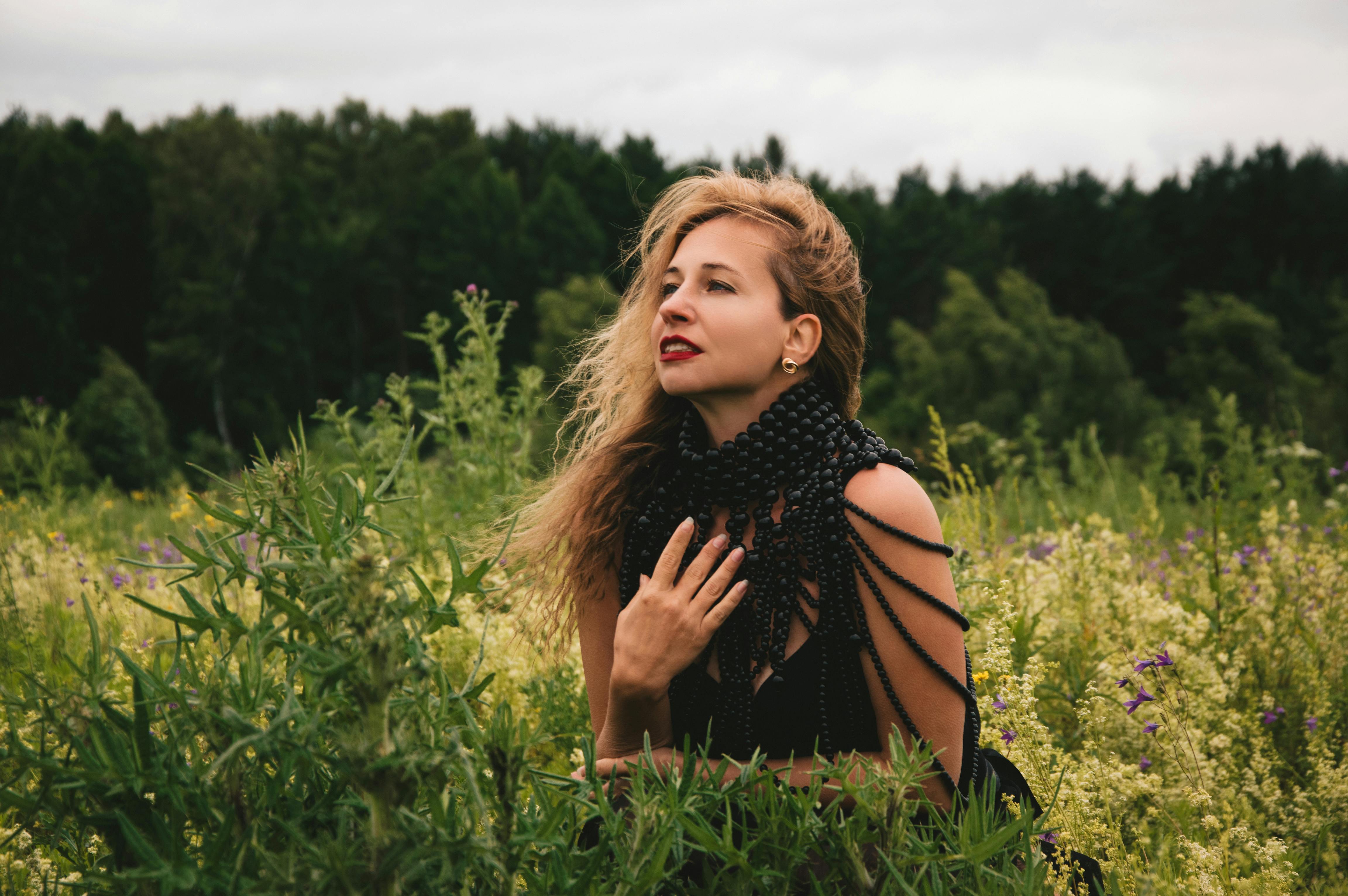 一位穿着黑色珠饰连衣裙的妇女在郁郁葱葱的绿色田野上摆姿势，背景是森林