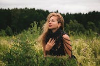 一位穿着黑色珠饰连衣裙的妇女在郁郁葱葱的绿色田野上摆姿势，背景是森林