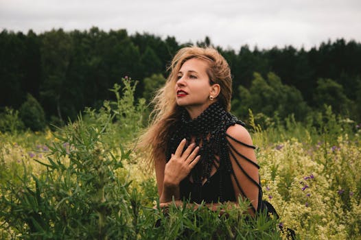 一位穿着黑色珠饰连衣裙的妇女在郁郁葱葱的绿色田野上摆姿势，背景是森林