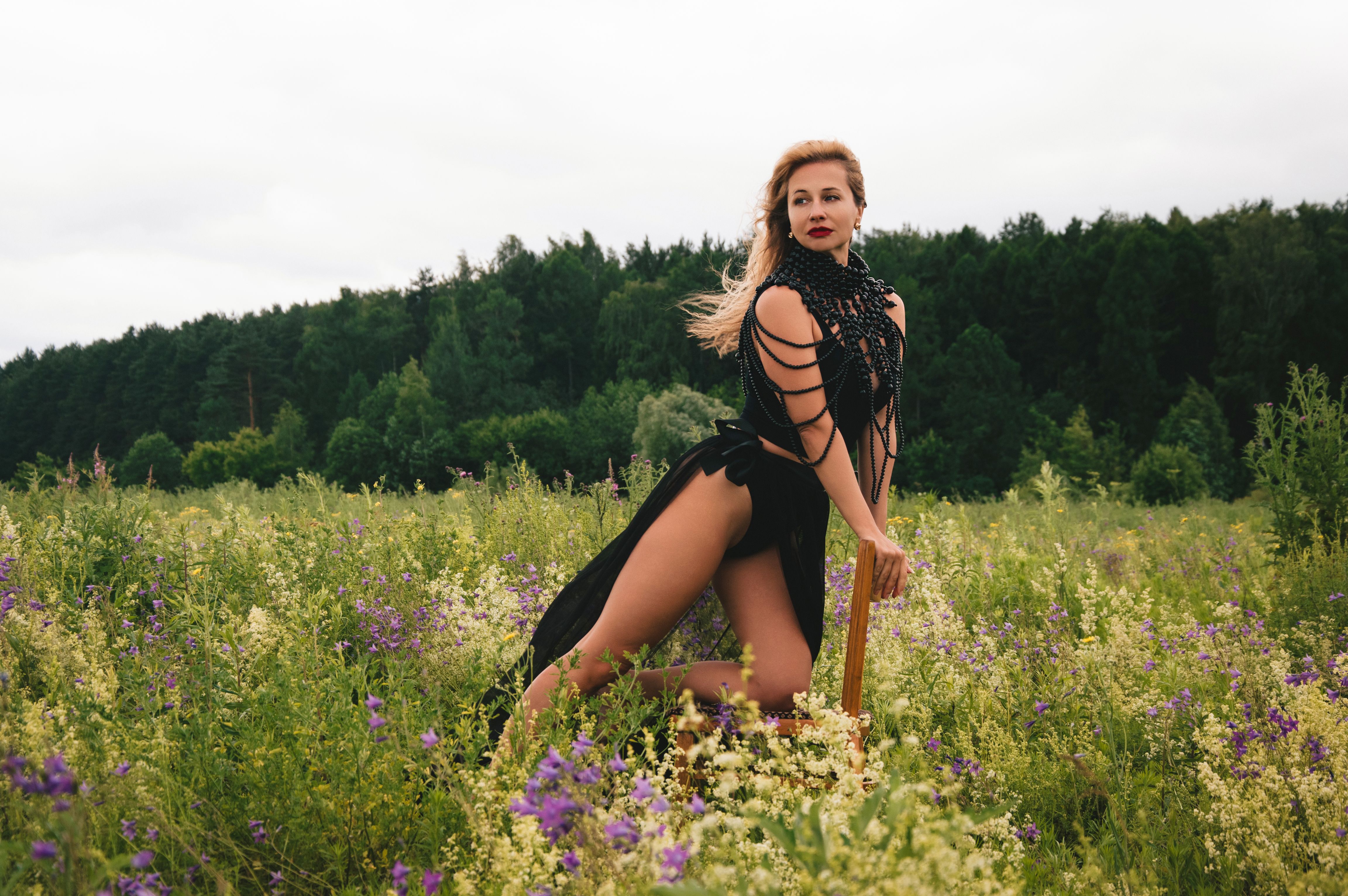 A woman in a stylish black dress poses confidently in a lush field with colorful wildflowers.