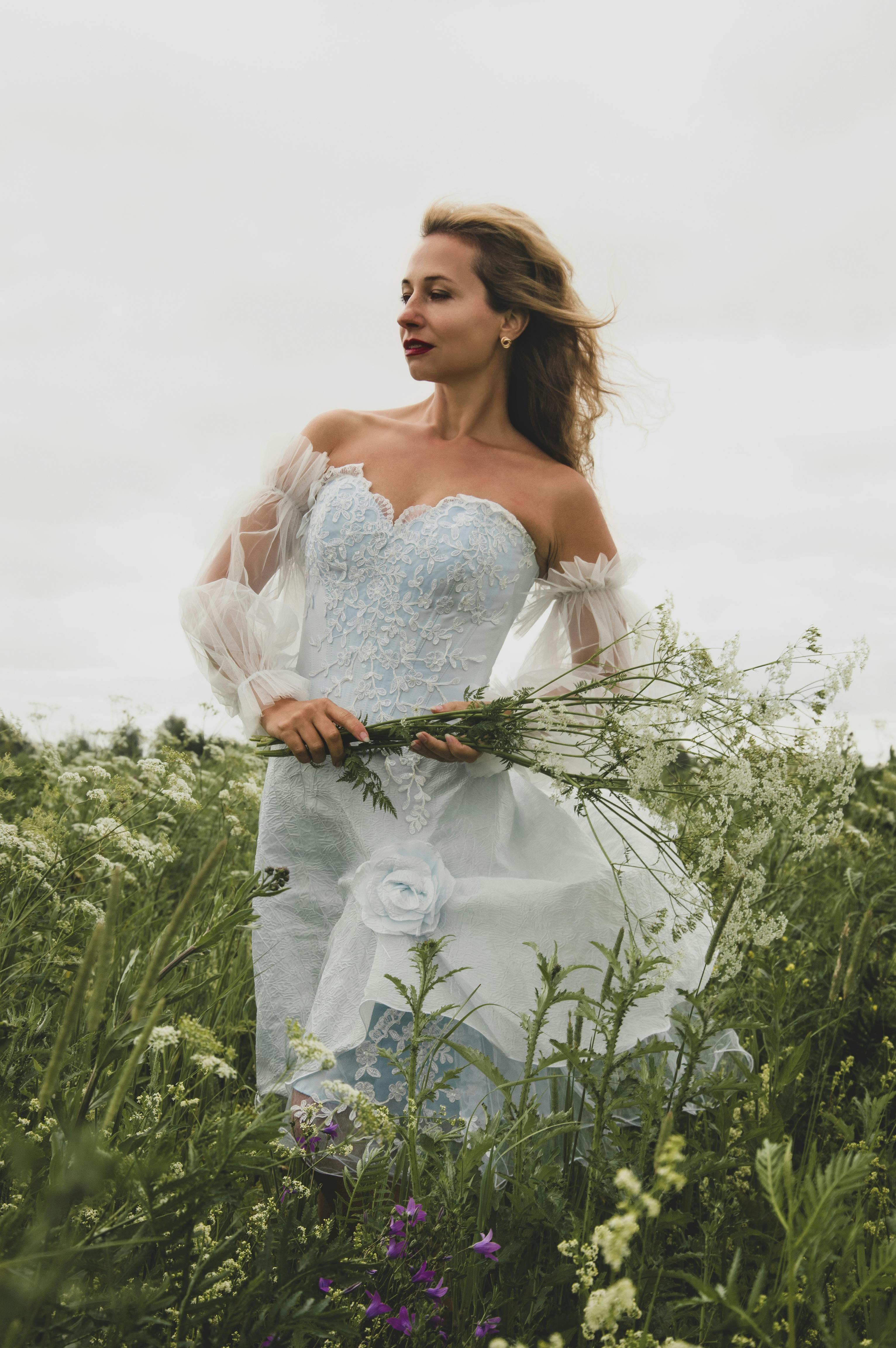 身穿蓝色蕾丝婚纱的女子站在野花田里，拥抱大自然