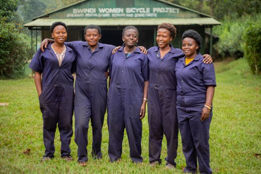 Five women in overalls at Bwindi Women Bicycle Project show empowerment and teamwork.