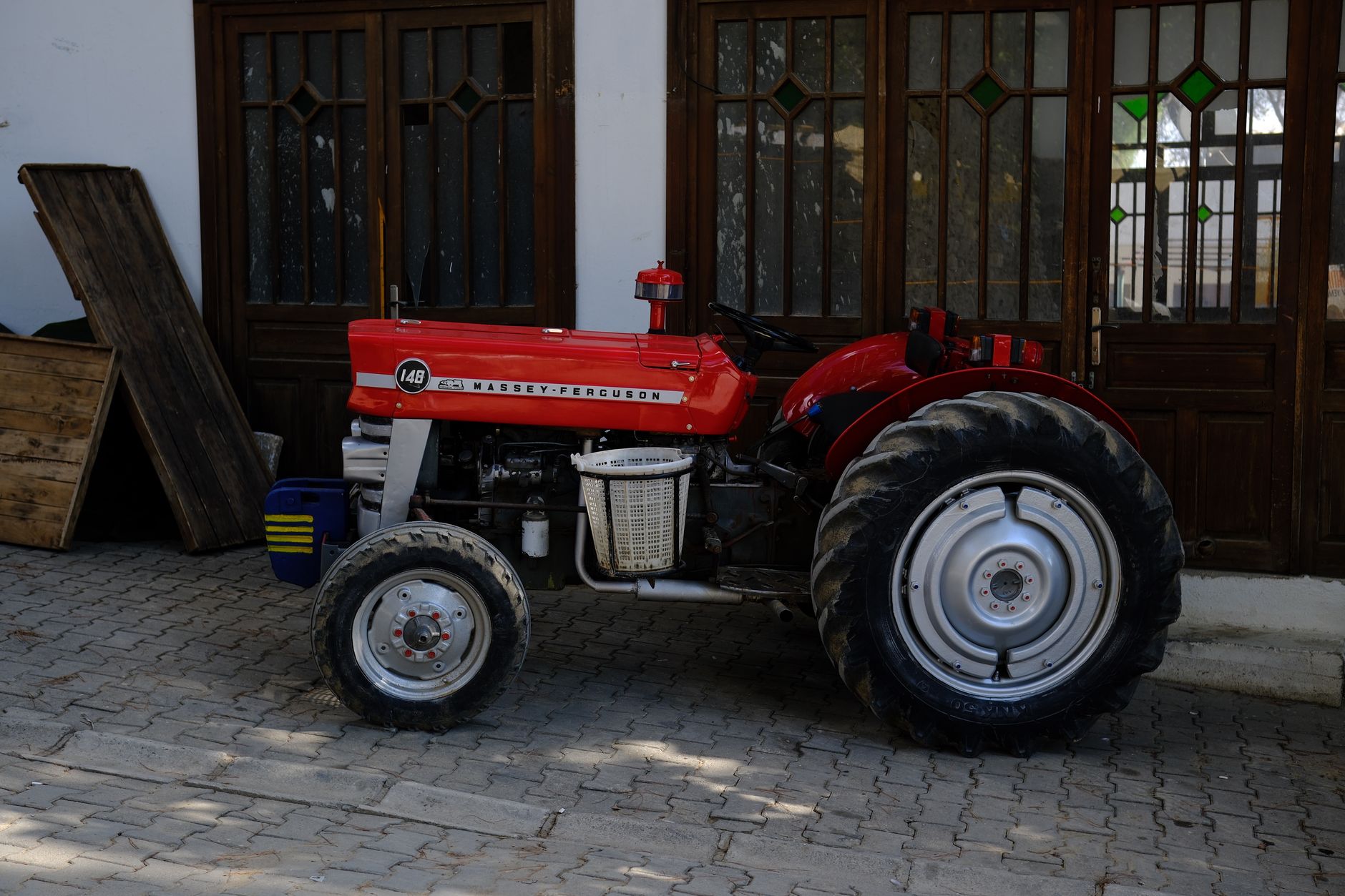 Red Massey Ferguson tractor parked outside with wooden doors in the background.