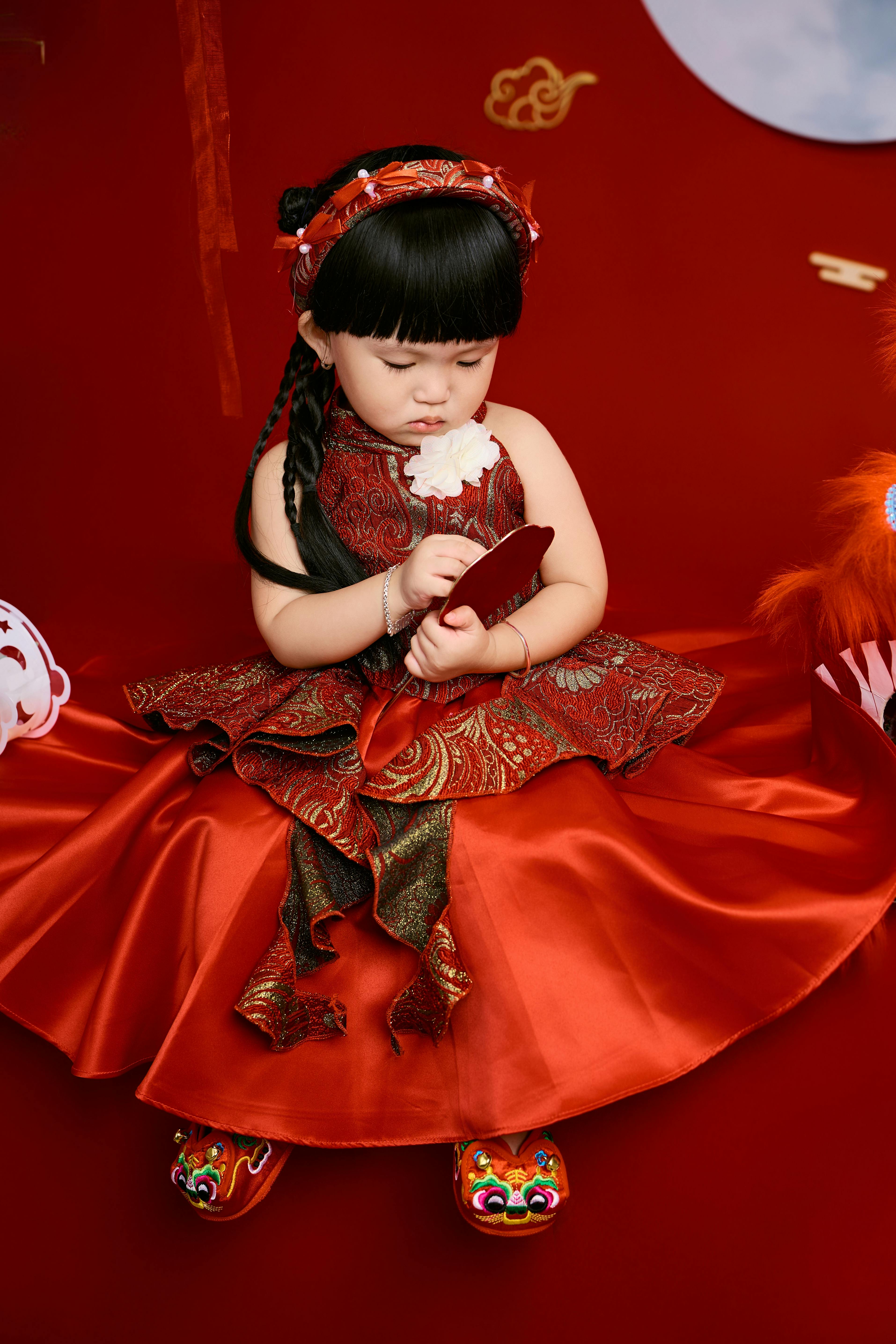 [ColoSach]-adorable-child-in-vibrant-red-traditional-asian-attire-holding-a-mirror,-celebrating-lunar-new-year.