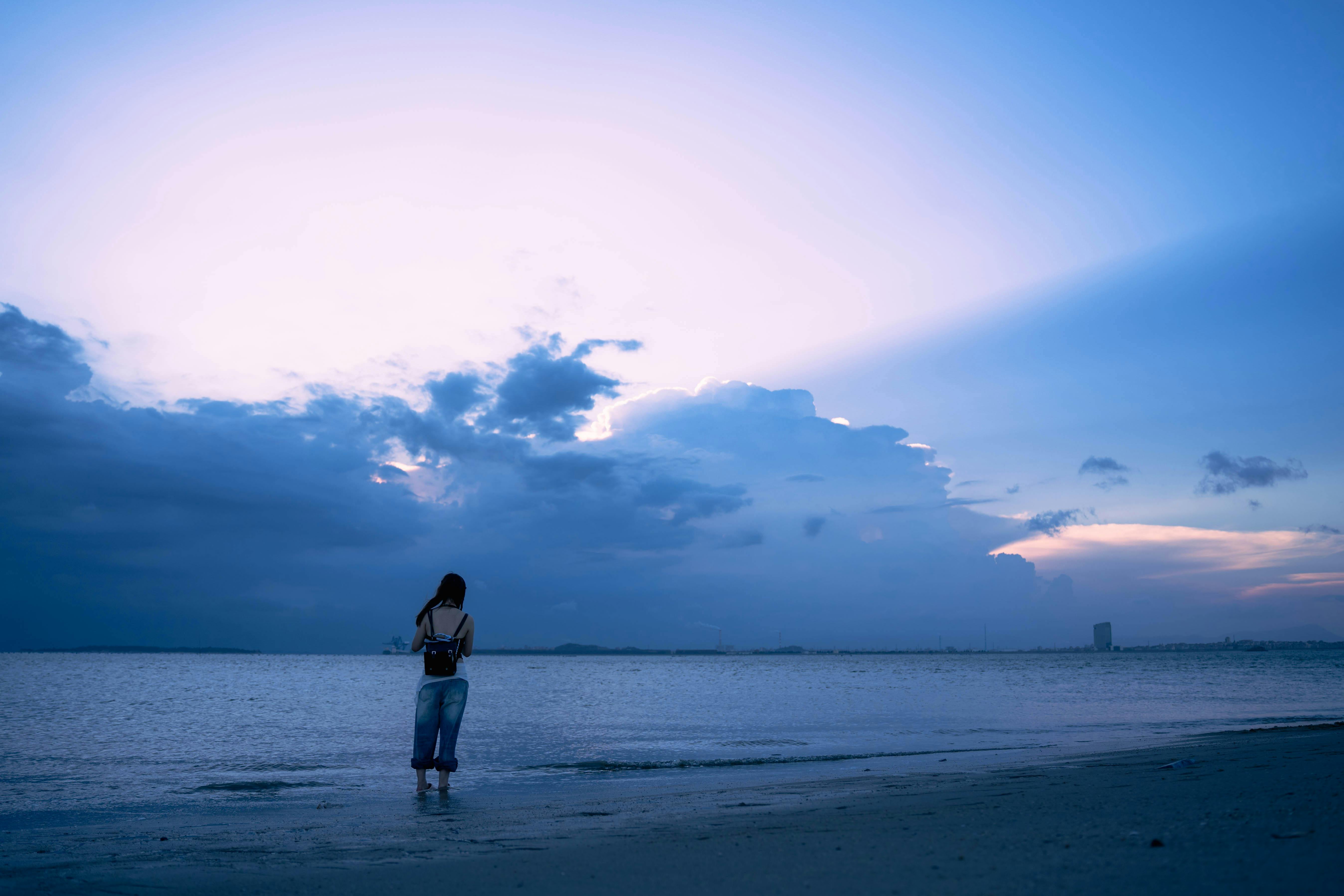 在黄昏时分，一名女子站在宁静的海滩上，她被天空和云层的美丽所惊叹
