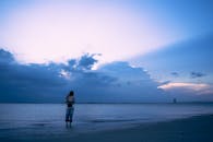 在黄昏时分，一名女子站在宁静的海滩上，她被天空和云层的美丽所惊叹