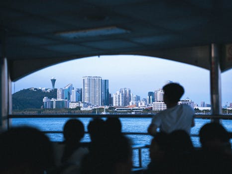 在渡轮上，乘客们的剪影映照在水面上，俯瞰着城市天际线