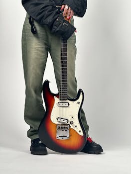 Electric guitar with sunburst finish held by casually dressed individual in studio setting.