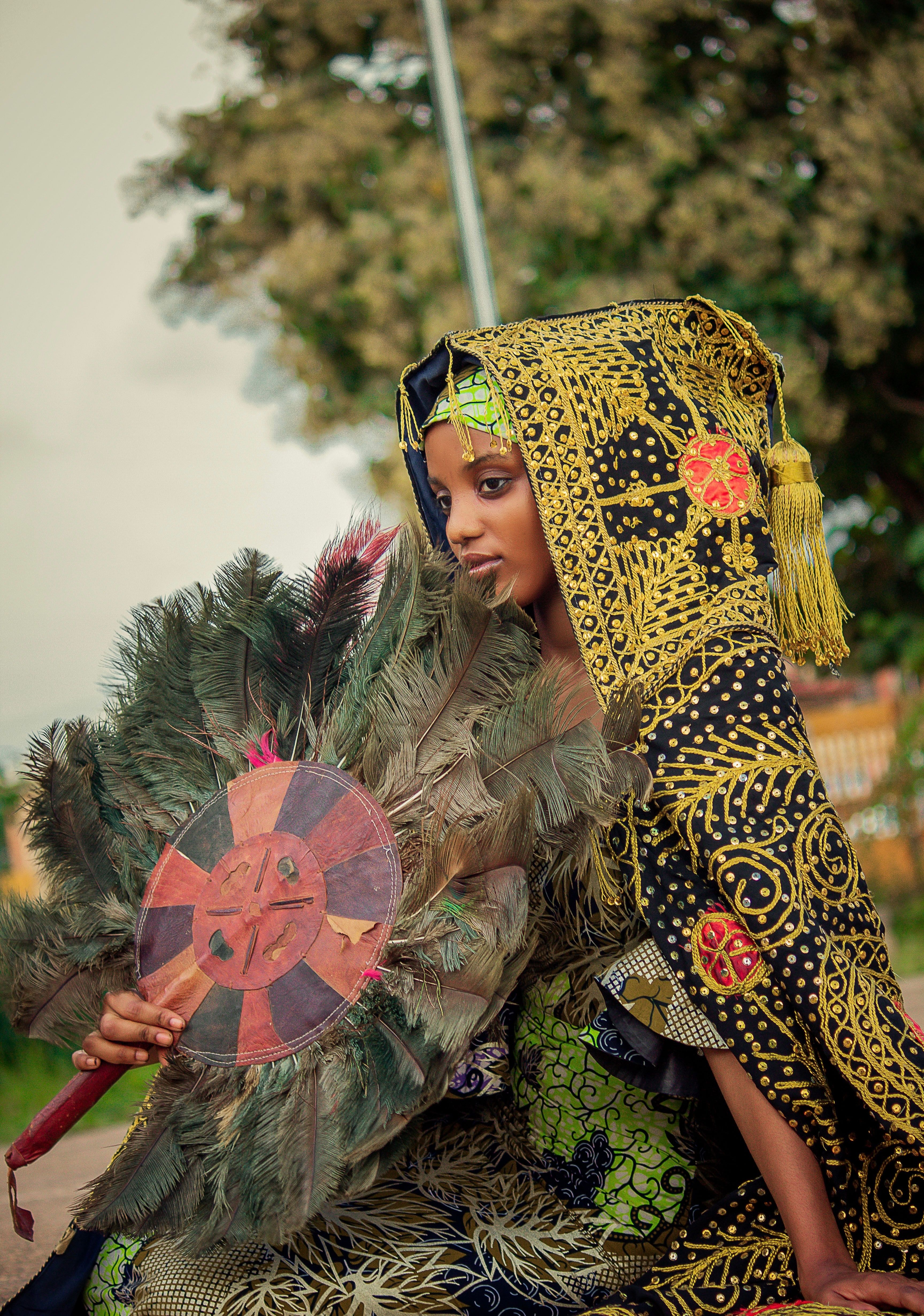 Beautiful African woman in traditional clothing, holding a colorful fan outdoors.