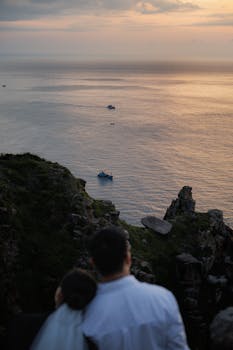在悬崖上，一对夫妇拥抱着，俯瞰着宁静的日落海景