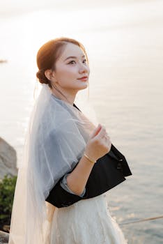 在日落时分，新娘戴着精致的面纱，穿着优雅的连衣裙，在海边优雅地摆姿势