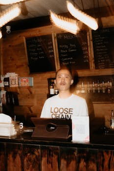 Barista behind the counter of a rustic coffee shop, surrounded by wooden decor and blackboards.
