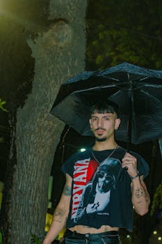 A stylish young man stands under an umbrella at night during a rainstorm in Argentina.