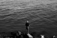 在海边岩石上，一名男子正专注地钓鱼，形成一幅黑白剪影的画面