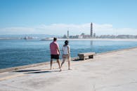 一对夫妇沿着海滨散步，远处的灯塔和清澈的蓝天