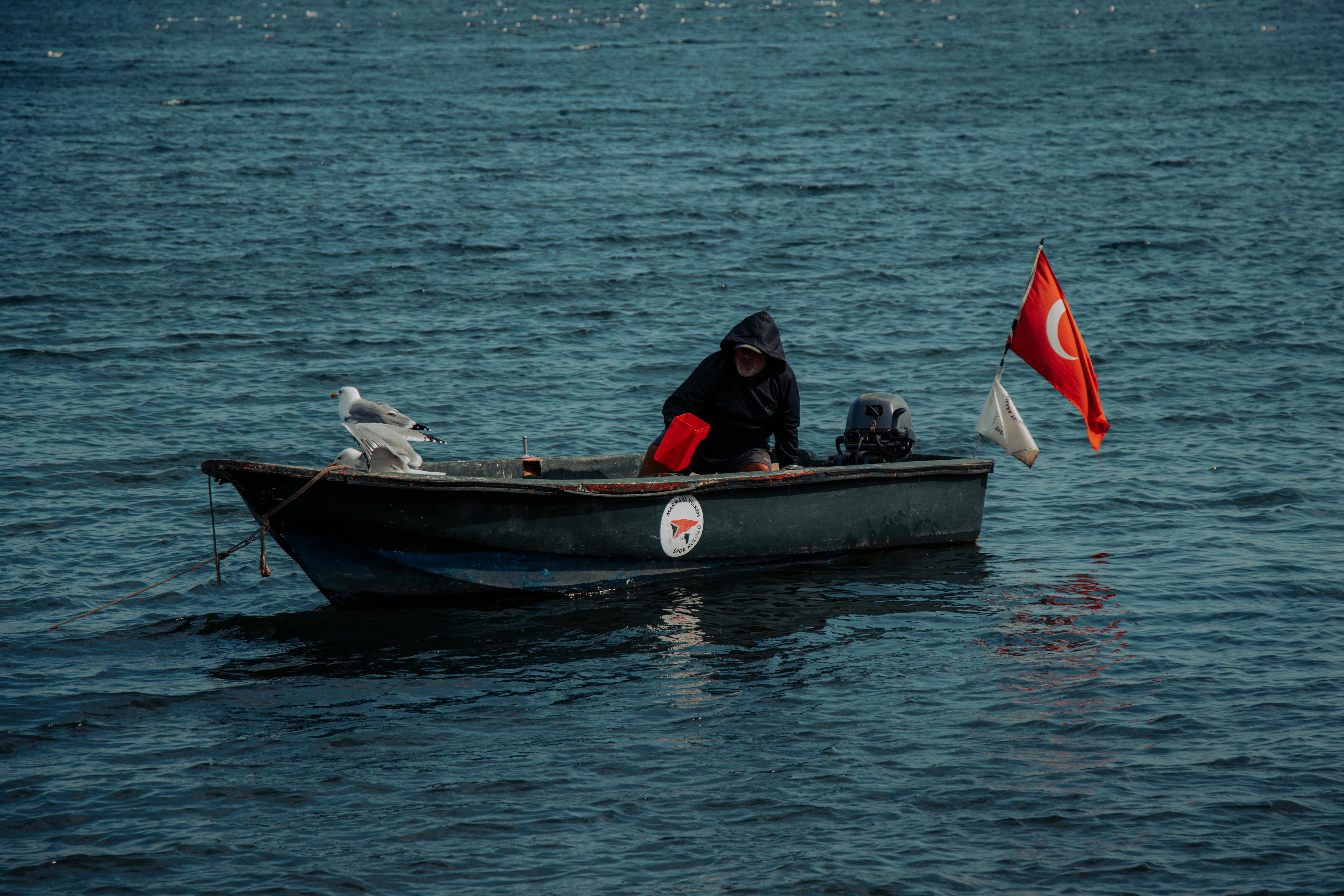 在伊斯坦布尔博斯普鲁斯海峡上，一艘小渔船上有一只海鸥和土耳其国旗