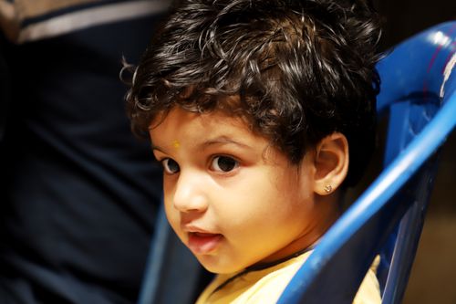 Free Close-up portrait of a young child with curly hair and curious expression, sitting on a blue chair. Stock Photo
